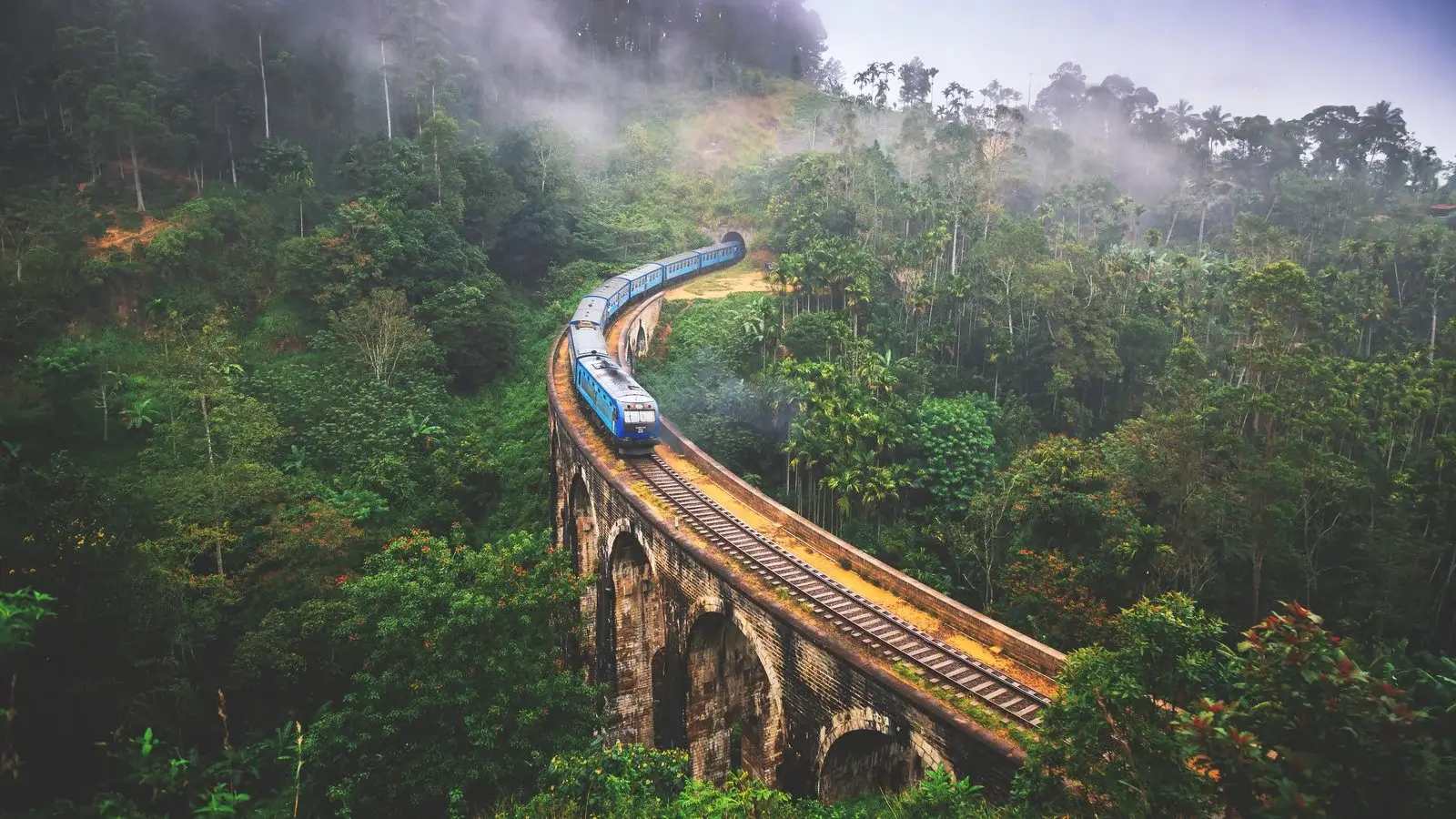 A blue train crossing Nine Arch Bridge amid Sri Lanka’s green hill country