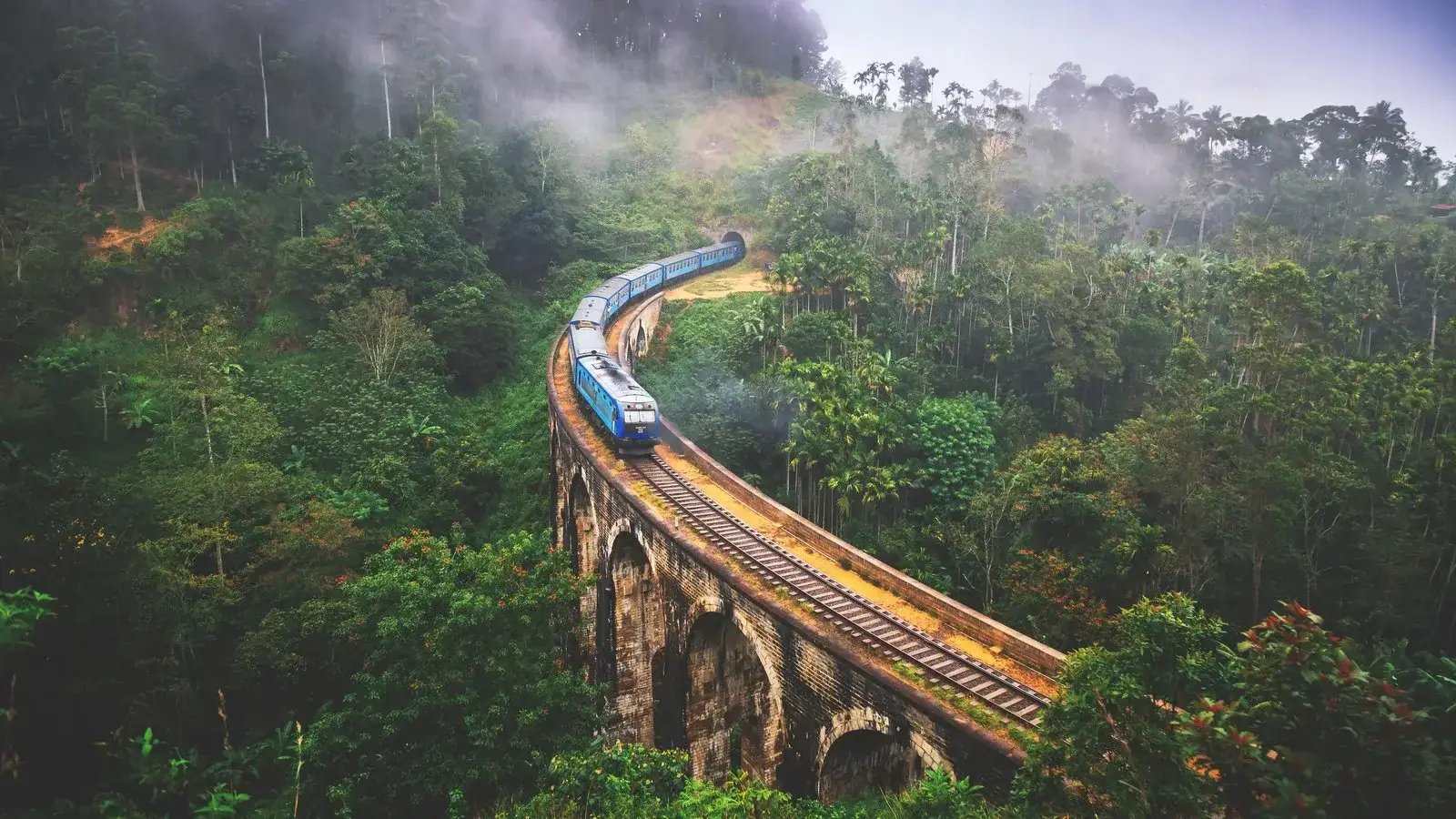 A blue train crossing Nine Arch Bridge amid Sri Lanka’s green hill country